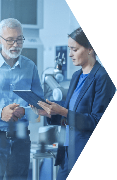 Two business professionals standing side by side in a lab and both looking down at a tablet.