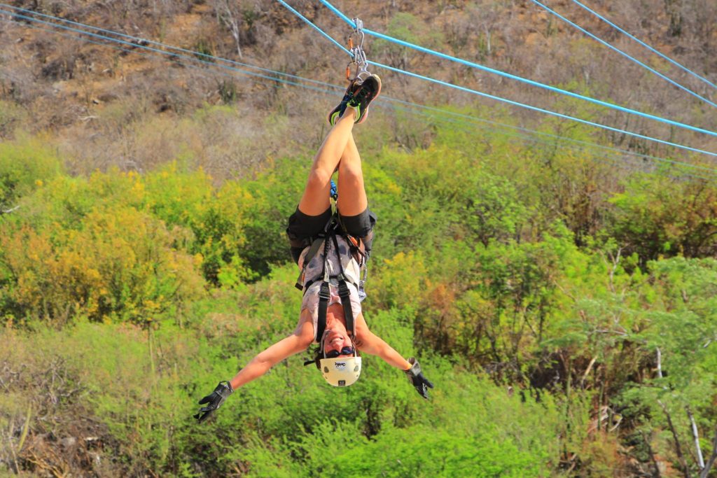 Photo of Christie hanging upside down from a zip line surrounded by greenery in the background