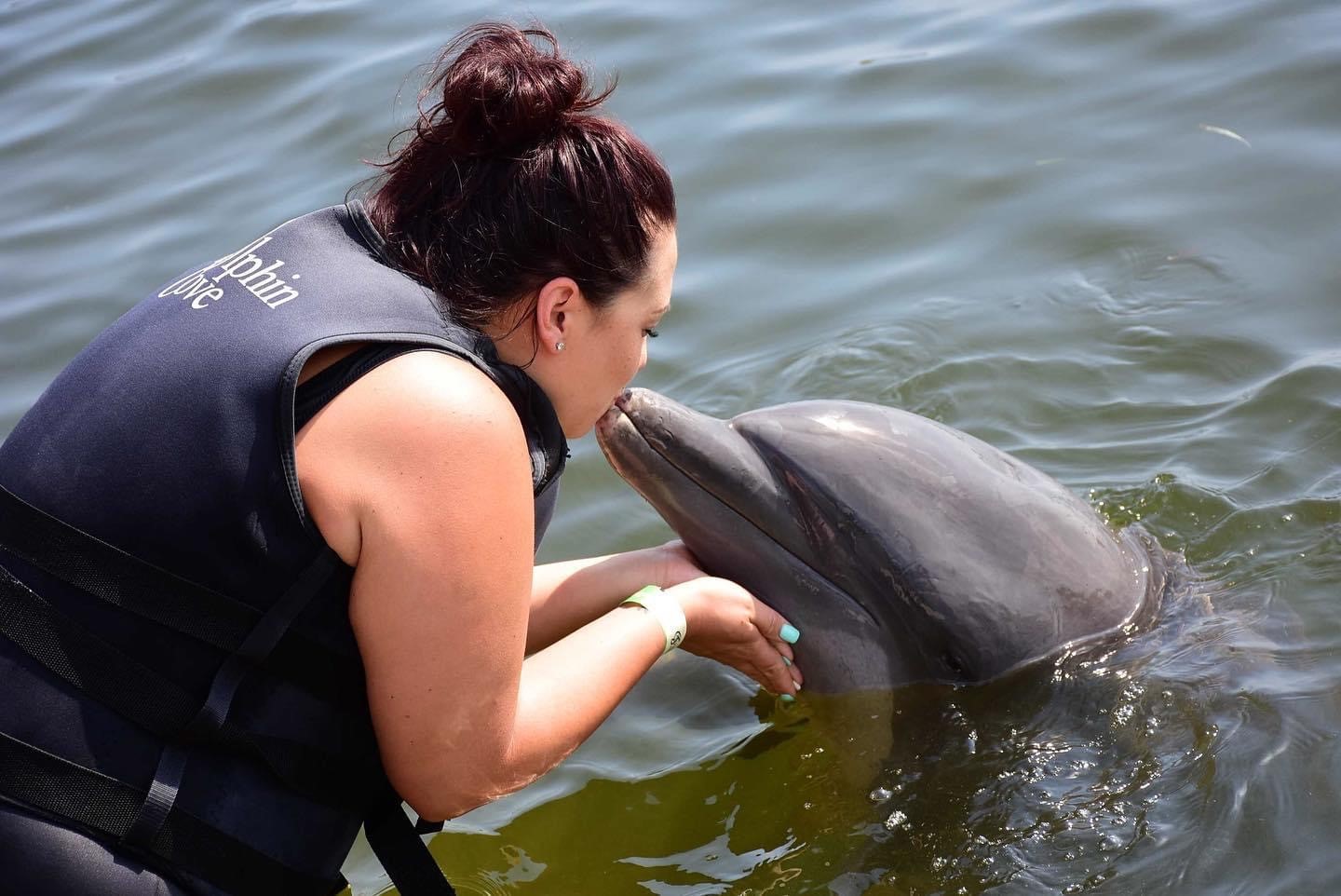 Brittany, wearing a life preserver, kisses a dolphin