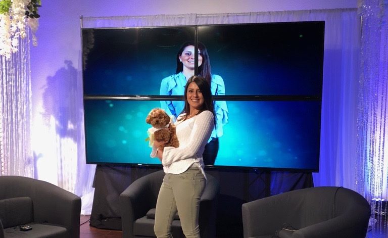 Bianka standing in front of a large screen TV holding her poodle