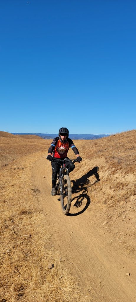 Bob on a mountain bike on a dirt trail with a blue sky in the background